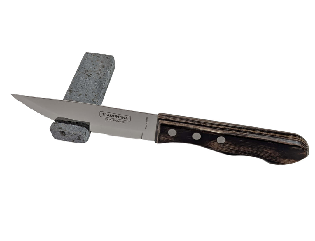 A Black Rock Grill Lava Rock Knife Rest – Limited Edition Table Accessory, featuring a stainless steel knife with a dark wooden handle balanced on a rectangular volcanic lava stone, isolated on white.
