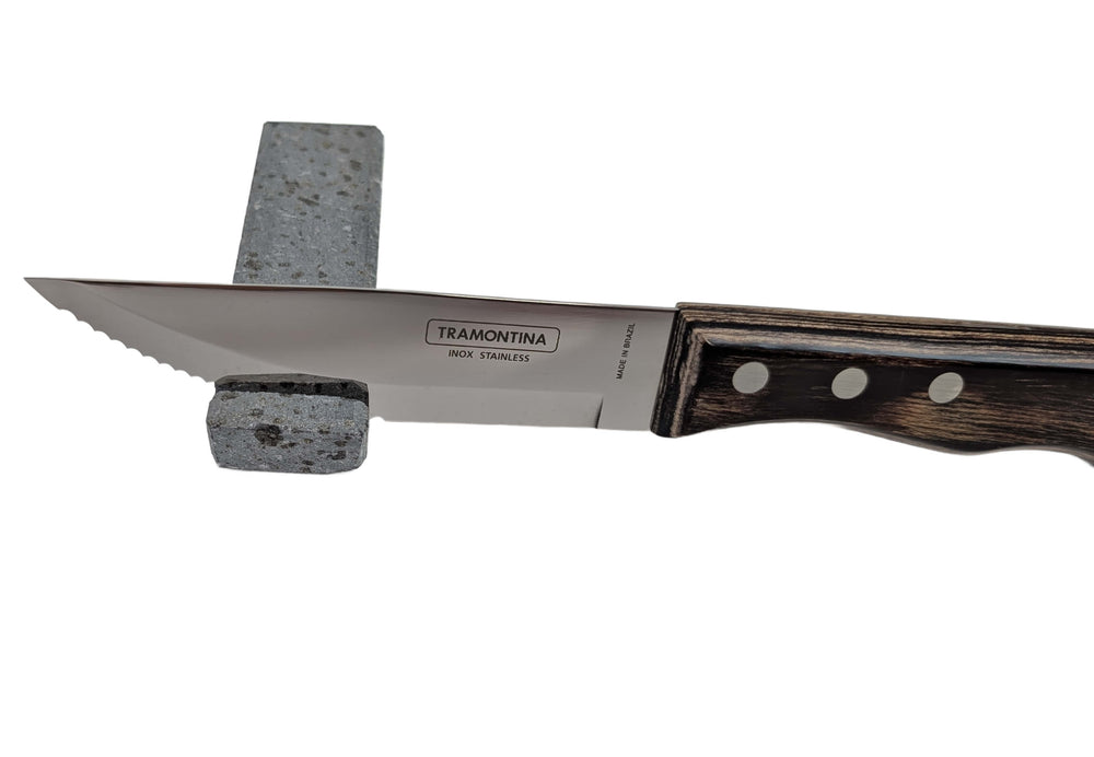 A Black Rock Grill Stone Knife Rest – Limited Edition Table Accessory balances a stainless steel kitchen knife with a wooden handle on a rectangular volcanic lava stone block against a white background.