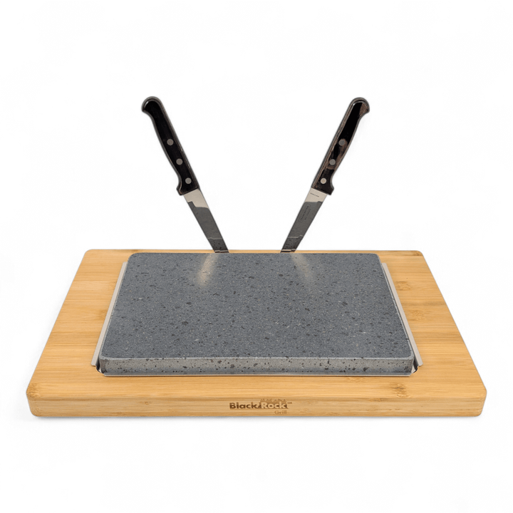 The Black Rock Grill Large Lava Sizzler Finishing Warming Platter features a rectangular board with a natural lava stone centerpiece and two kitchen knives standing upright in the slab, displayed against a white background.