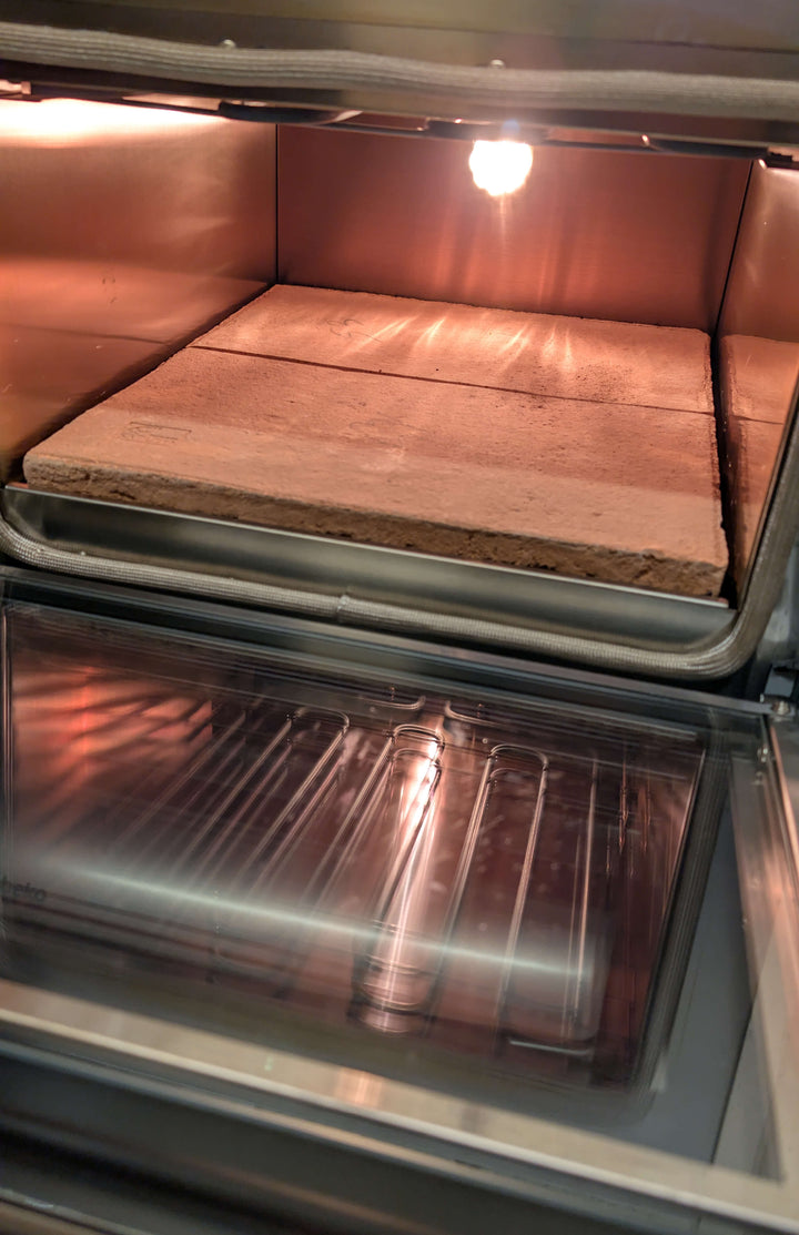 The Macte Voyager Twin Electric Pizza Oven by Macte, AVPN certified, features an open door revealing a heated baking stone on the middle rack and a metal rack below, both brightly lit—ideal for authentic professional pizza results.