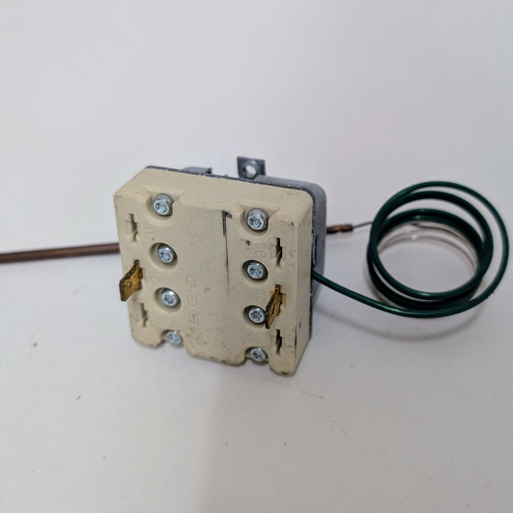 A Black Rock Grill Effeuno 515°C Overheat Reset Switch for P134H/P134HA (450°C, 500°C, 509°C) is shown with a beige rectangular body, visible screws and metal prongs, attached to a coiled green wire and thin metal rod on a white surface.