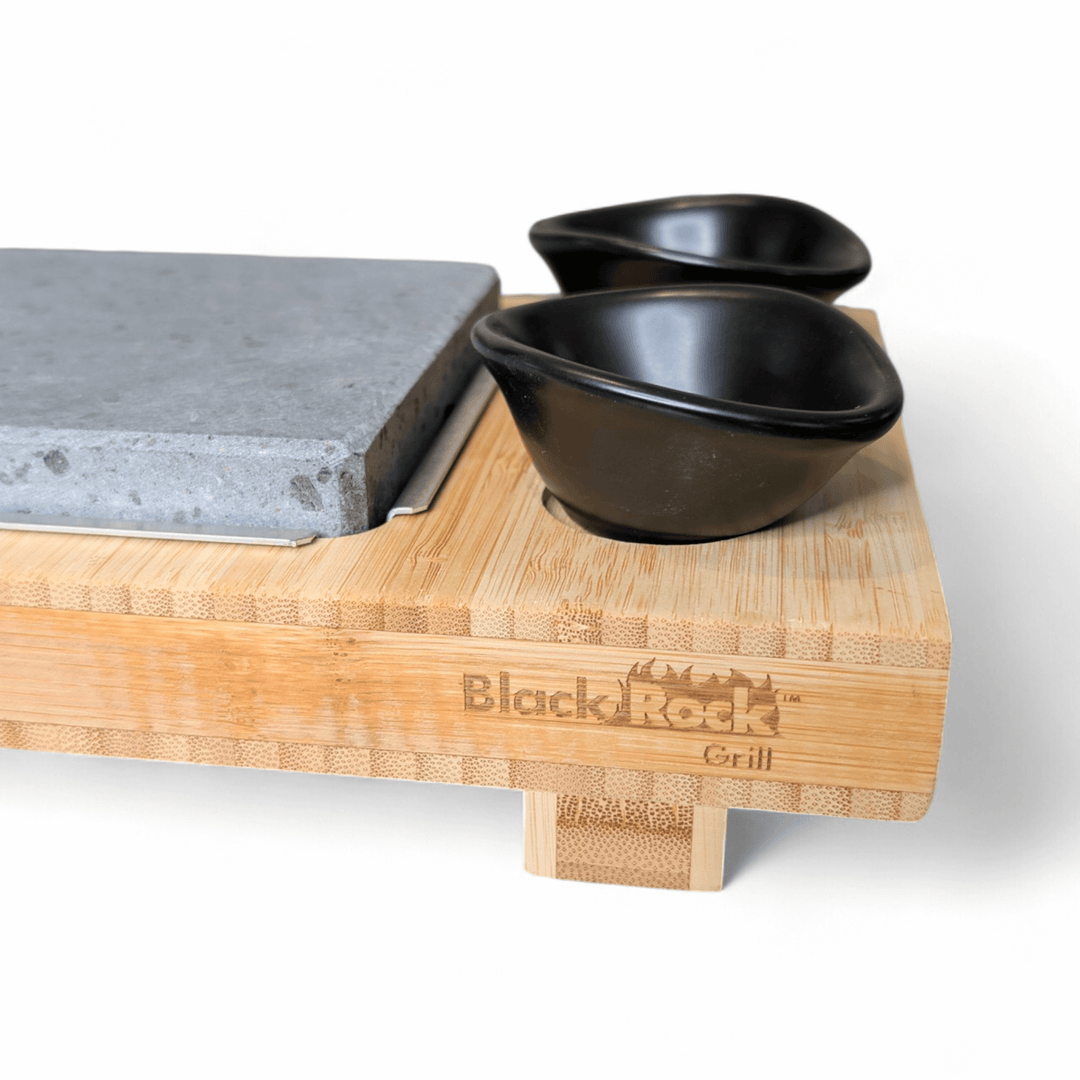 The Black Rock Grill Sharing Lava Sizzler Finishing Warming Platter features a bamboo board engraved with the brand, a natural lava stone slab, and two black dipping bowls—an ideal sizzling platter for your table.