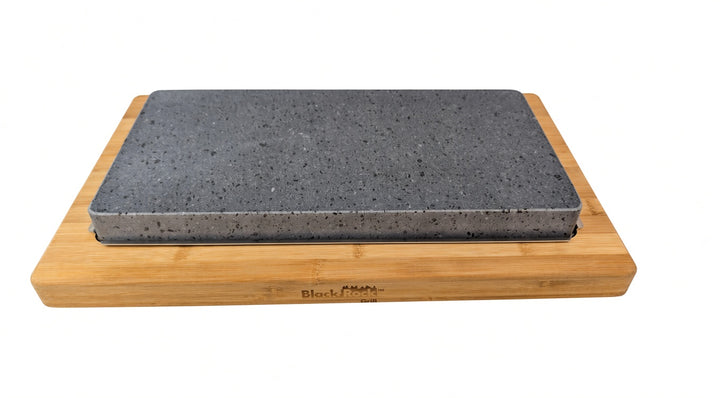 A rectangular grey lava cooking stone, resting on a light natural bamboo cutting board, shown against a plain white background.