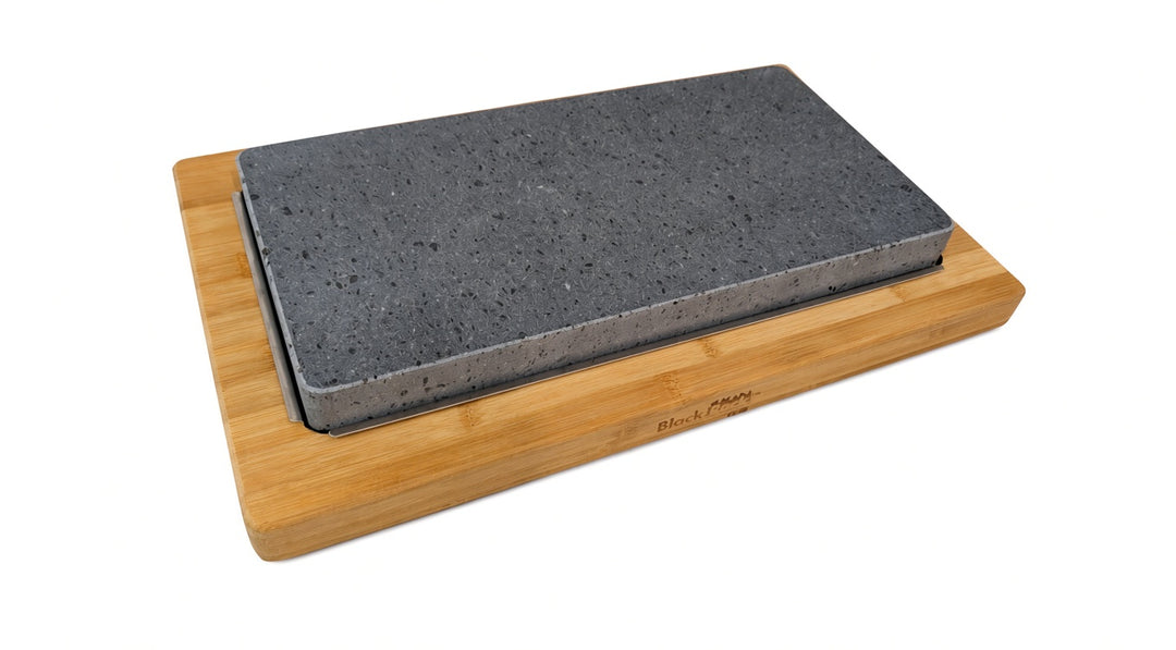 A rectangular dark gray lava cookinf stone resting on a light natural bamboo block, photographed on a clean white background.
