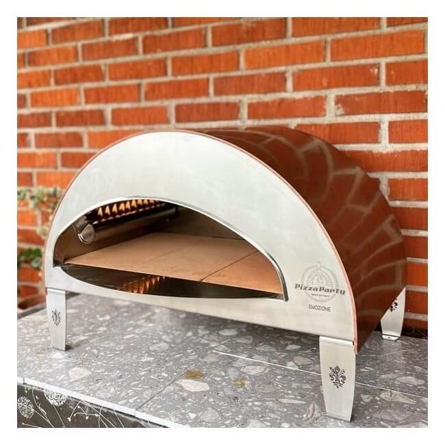 Angled view of a copper Pizza Party Emozione pizza oven set up outdoors in a garden.