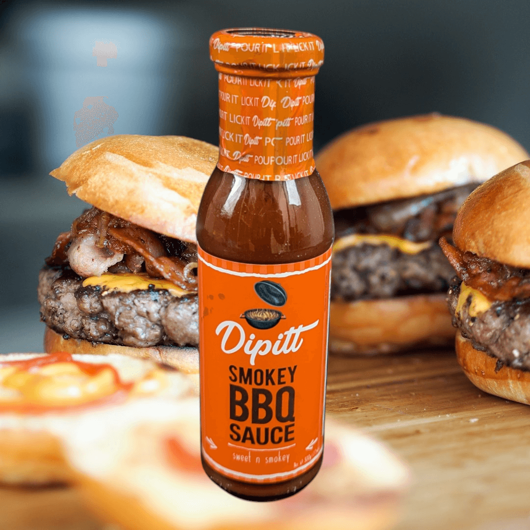 Dipitt Smokey BBQ Sauce, Sweet and smokey 300g glass bottle of sauce with burgers in the background
