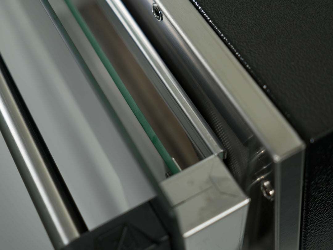 Close-up of a partially opened metal drawer with green-tinted glass, highlighting the sleek design and quality craftsmanship of the Effeuno Pulse Electric Pizza Oven—Made in Italy for perfect Neapolitan pizzas.