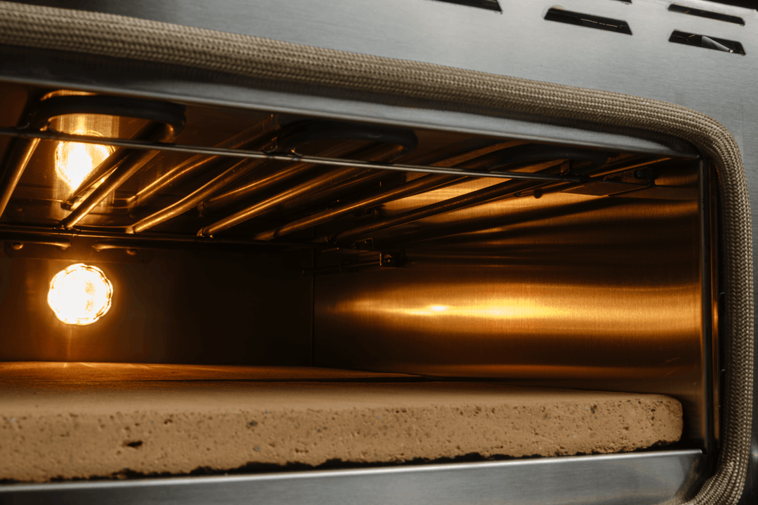 Inside the open Macte Voyager Twin Advanced pizza oven, showing the Biscotto refractory stone, top heating element, and interior lights.