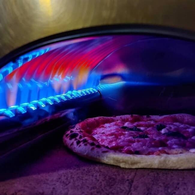 Pizza inside a glowing pizza party ardore gas pizza oven with a colorful flames.