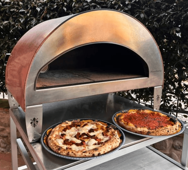 Two freshly cooked pizzas resting on a counter directly in front of the Pizza Party Emozione outdoor oven.