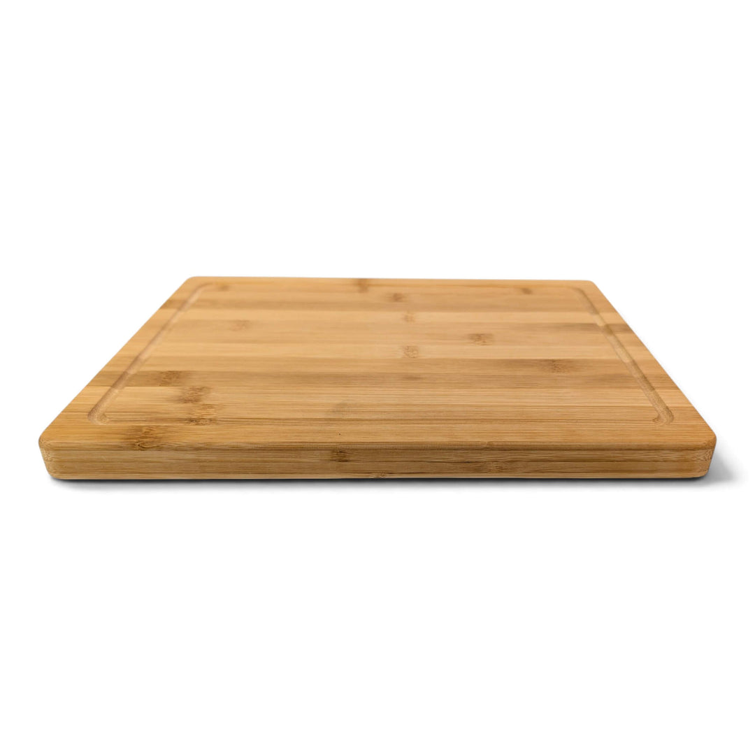 A single bamboo serving board with rounded corners and juice channel, shown from a slight angle on a white background.