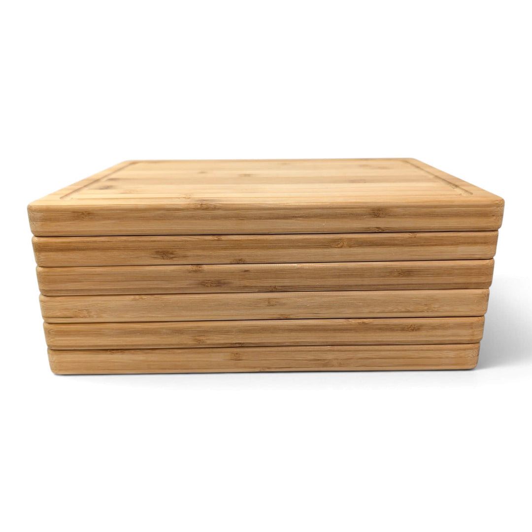 A stack of six rectangular bamboo serving boards with a juice channel stacked and shown on a clean white background.