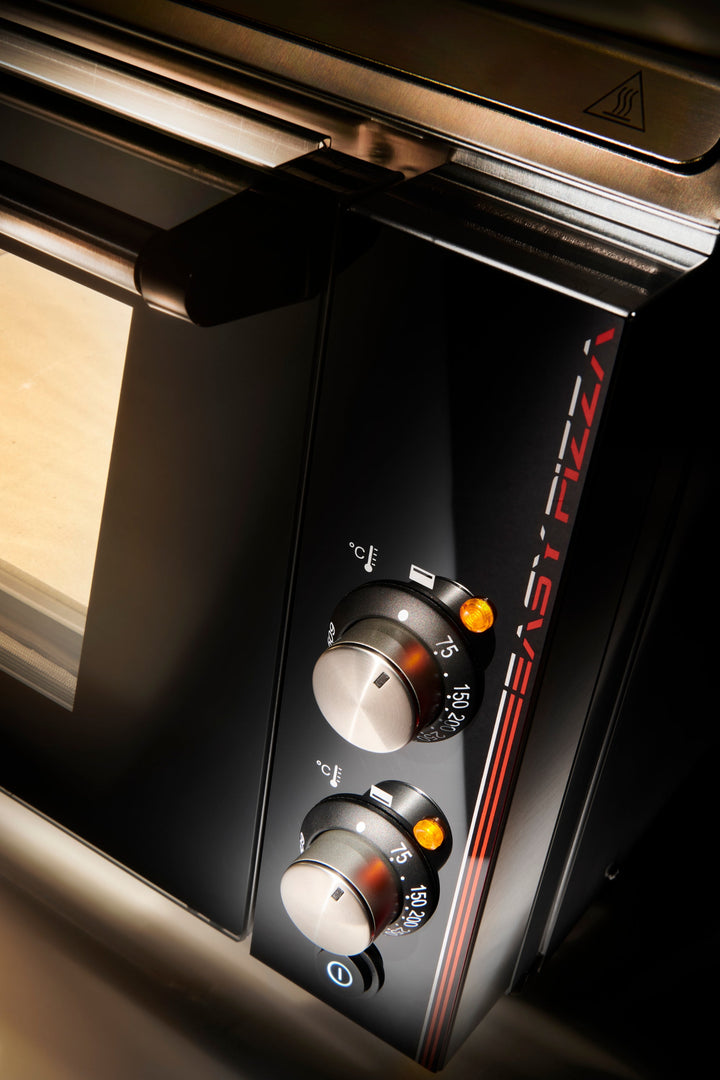 Close-up of the Black Rock Grill Effeuno P134H 509 Manual Pizza Oven, featuring two temperature control knobs, orange indicator lights, and a front panel—partially showing the door and handle. Perfect for Neapolitan-style pizza.