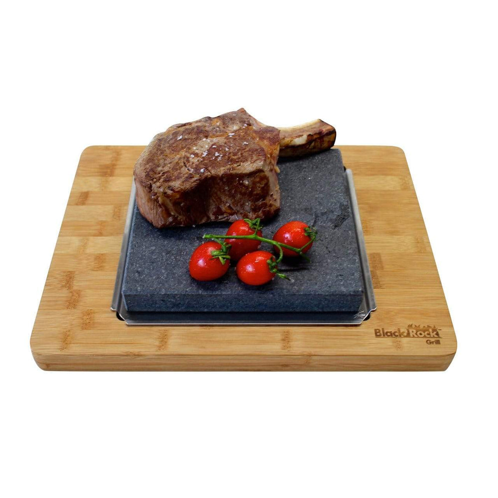 A grilled steak and cherry tomatoes sit on a rectangular black stone slab placed on a GP-3627 bamboo board, custom-engraved with Black Rock Grill in the corner.